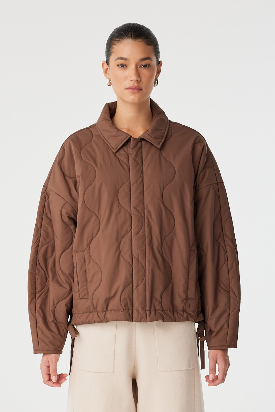 Model wears quilted espresso jacket with relaxed fit and concealed front placket.