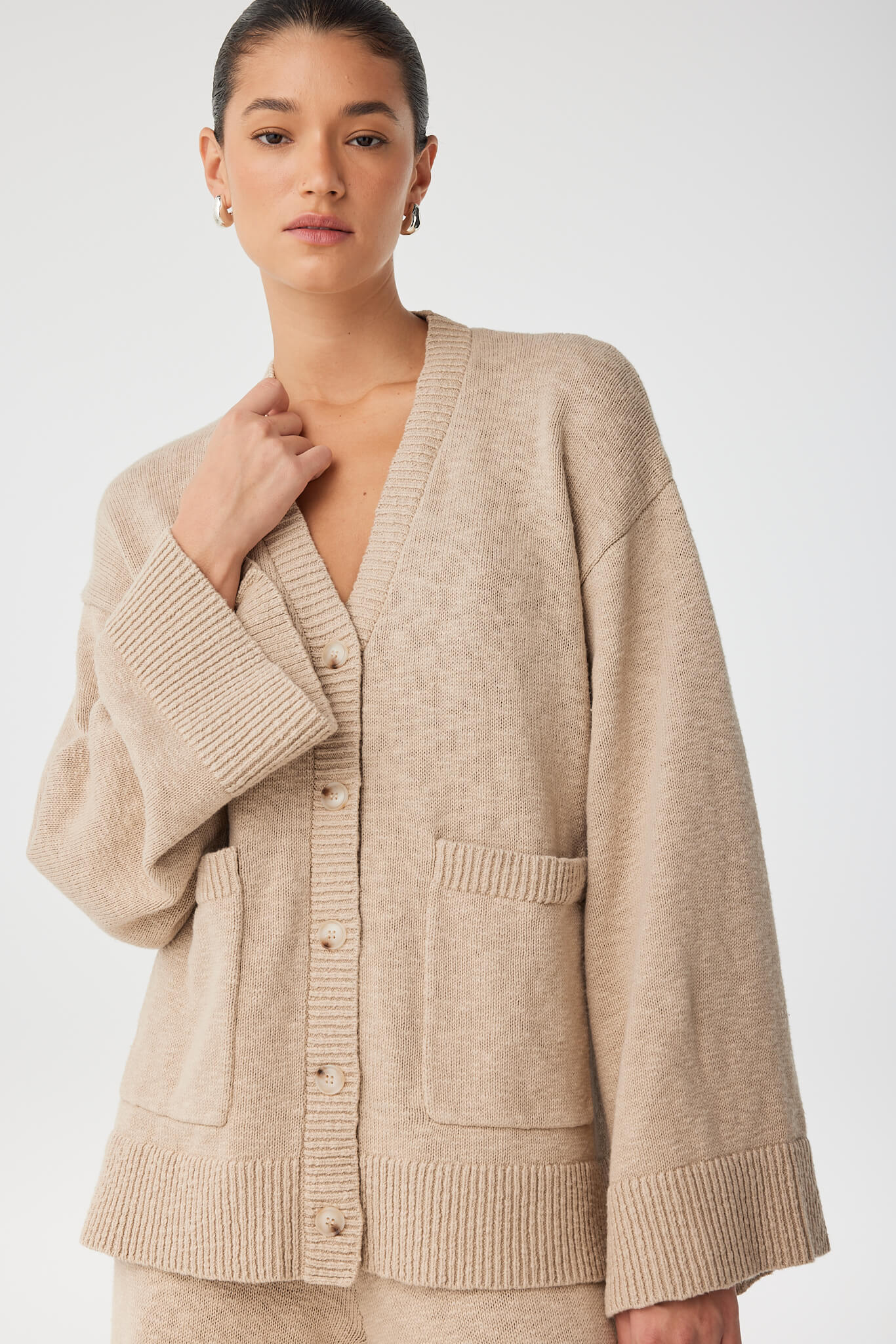 Model wears soft structured taupe cardigan with relaxed cut and subtle texture, ideal for everyday comfort.