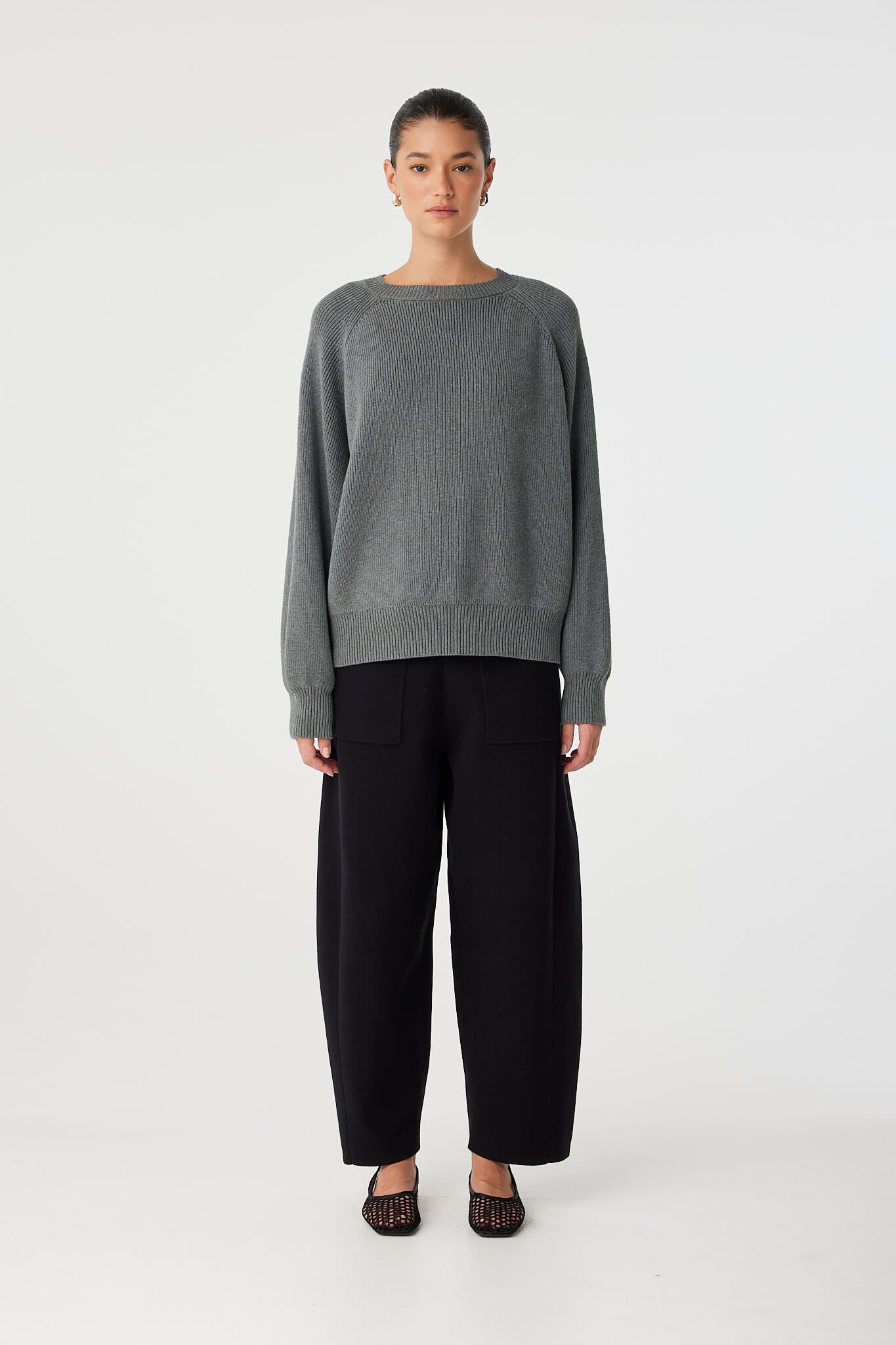 Full-body view of relaxed-fit grey sweater in organic cotton blend, styled with black pants.