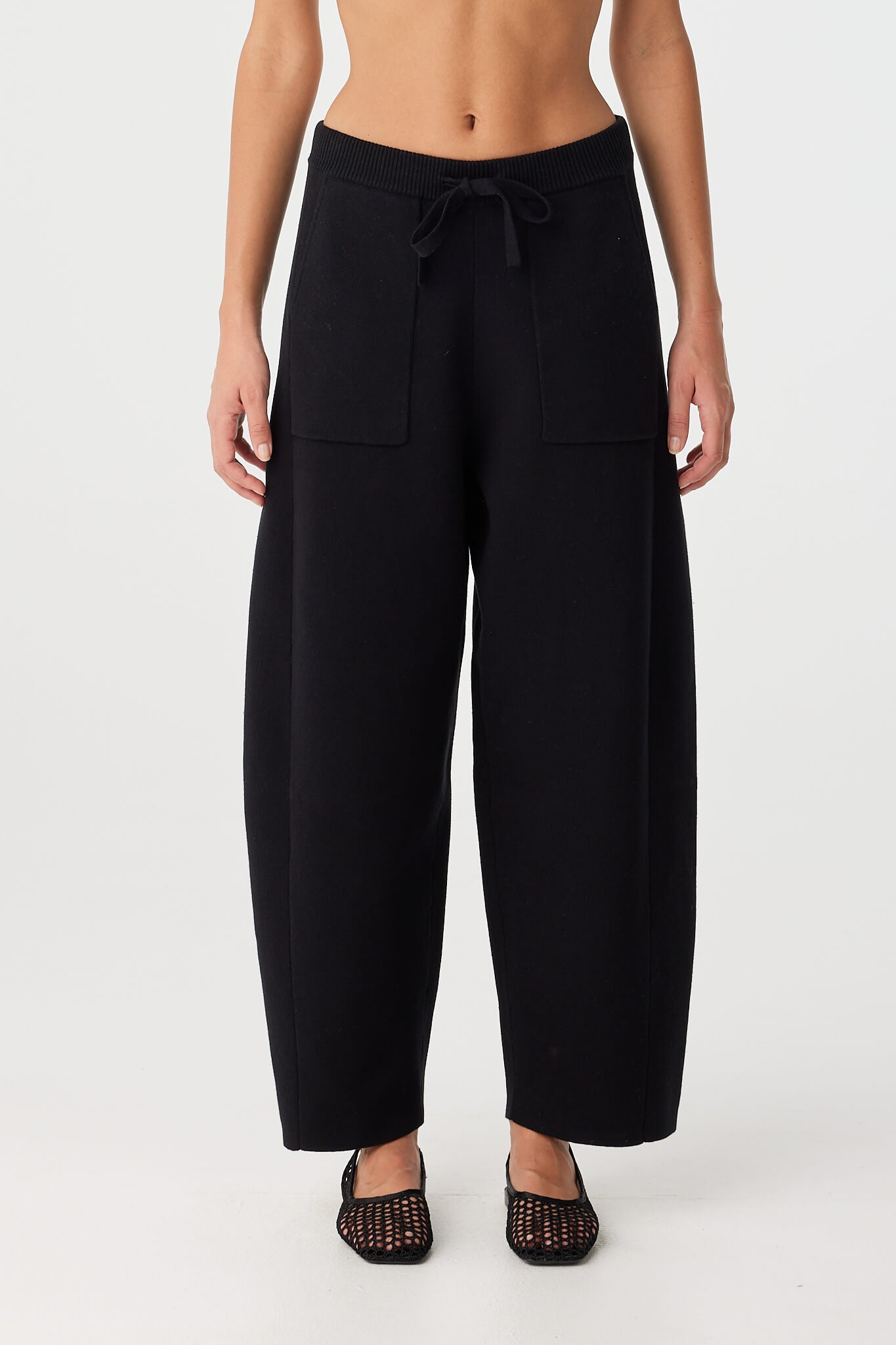 Model wears black barrel-leg knit pants with patch pockets and ribbed waistband.