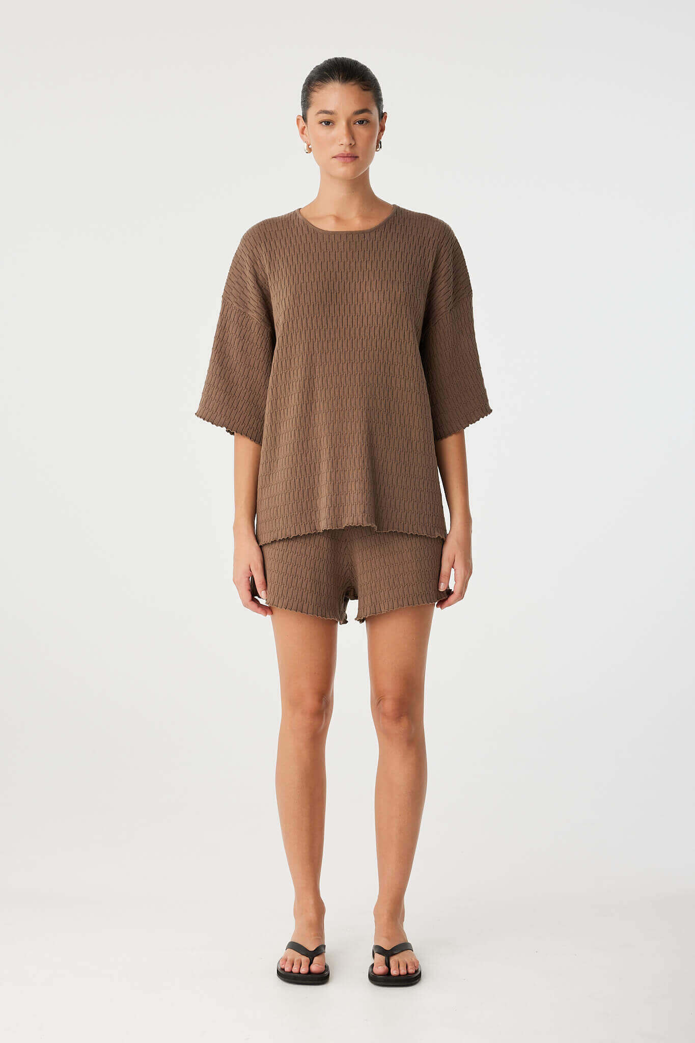 Model wears relaxed knit shorts and matching oversized tee in textured cacao cotton, styled for effortless layering or elevated loungewear.