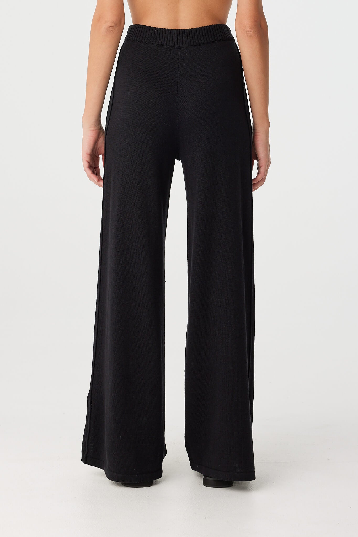 Back view of high-rise black pants with elastic waistband and wide-leg fall, designed for comfort and seasonal layering.