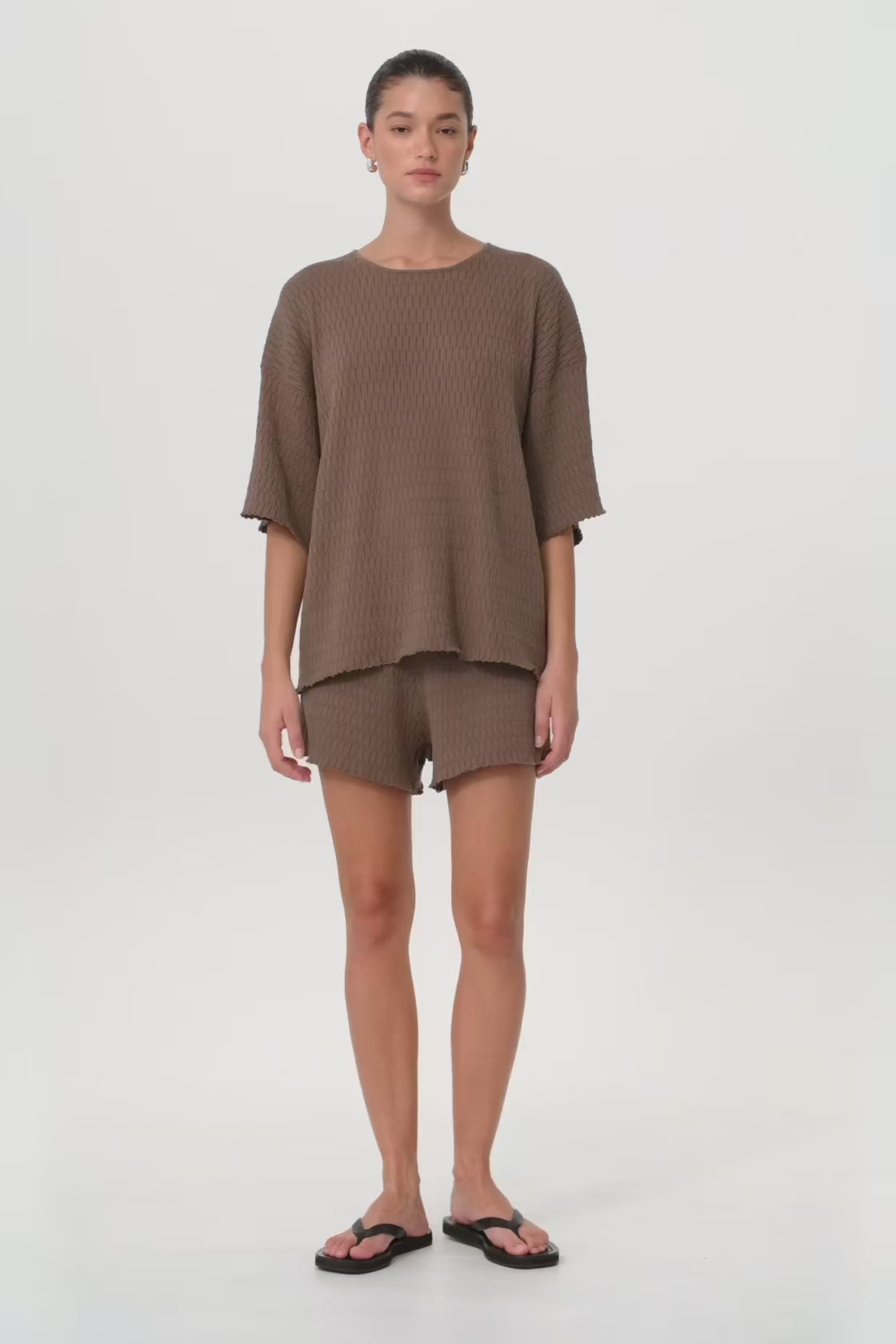 Model in motion wearing textured knit shorts and matching oversized tee, highlighting movement, rib structure, and breathable organic cotton, designed for ease through changing seasons.