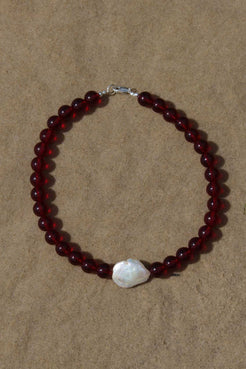 Red garnet beaded necklace with freshwater pearl focal bead, arranged in a circle on a warm beige background.