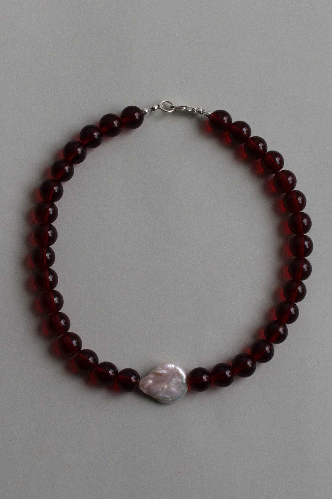 Red garnet beaded necklace with a single freshwater pearl centrepiece, laid flat on a soft grey background.