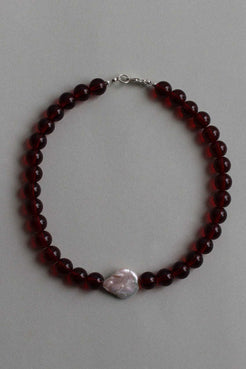 Red garnet beaded necklace with a single freshwater pearl centrepiece, laid flat on a soft grey background.