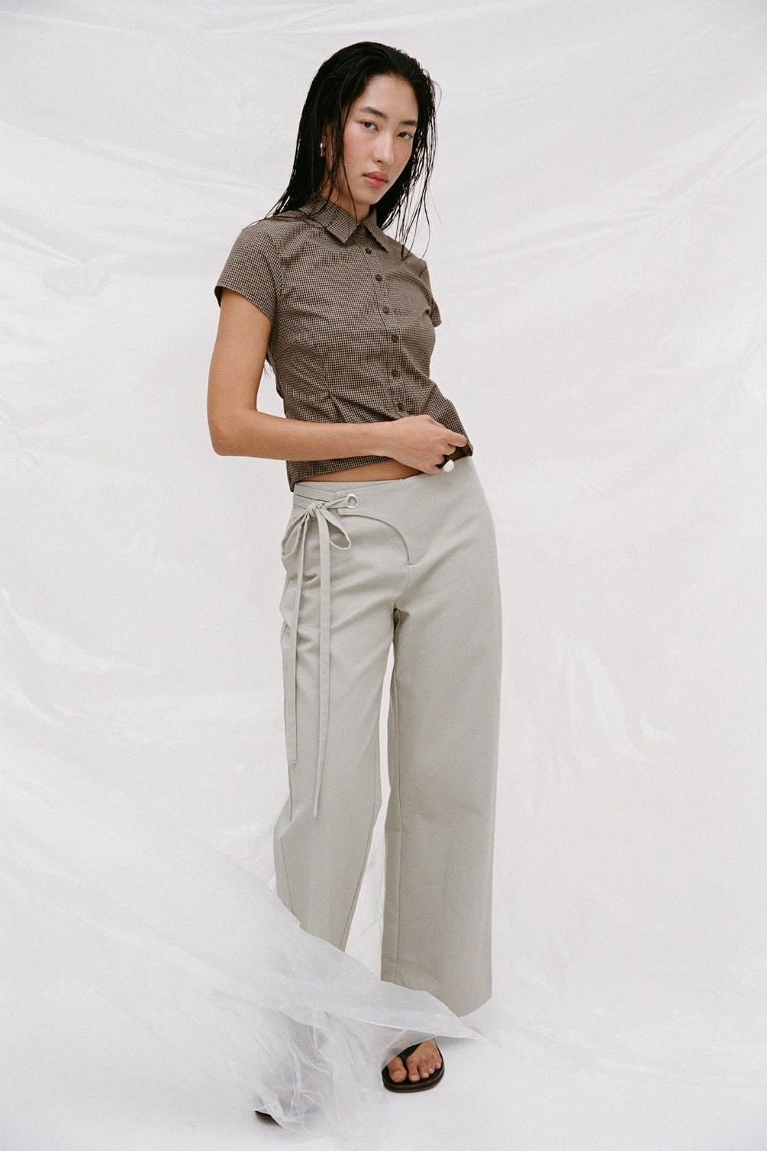 Model wearing lucia pants in light sage against a white studio background. Styled with freya shirt in chocolate check. 