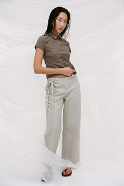 Model wearing lucia pants in light sage against a white studio background. Styled with freya shirt in chocolate check. 