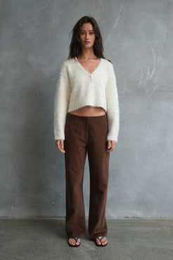 Model wearing the Avery Pant in Espresso, showcasing the full-length straight-leg fit and rich espresso tone, paired with a cream fluffy cropped cardigan against a textured concrete backdrop.