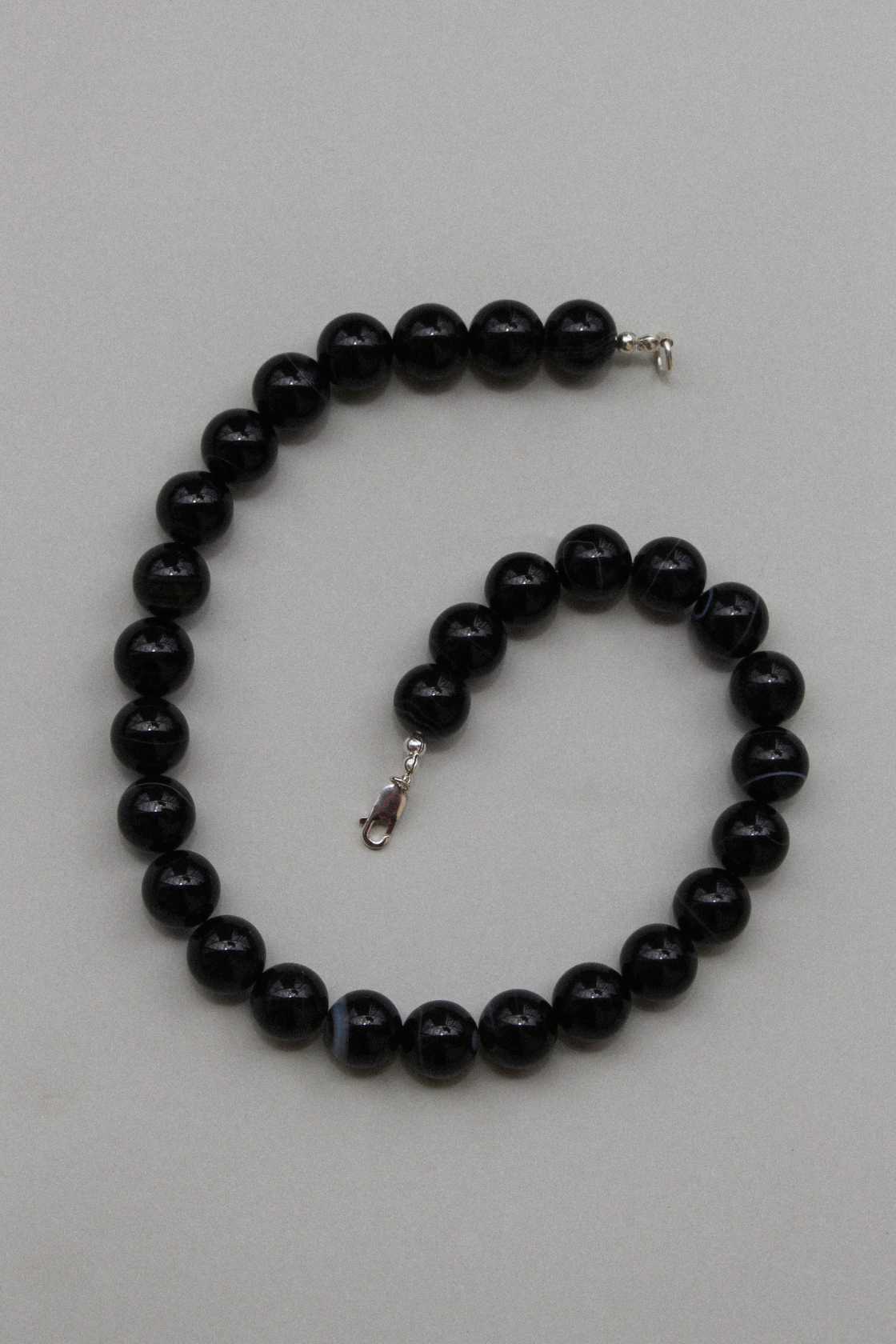 Black agate gemstone necklace shown in a gentle curve, highlighting the round beads and silver clasp on a neutral surface.