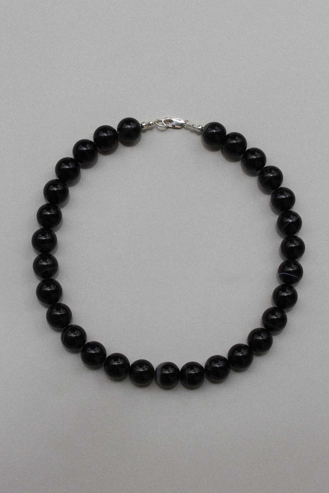 Black agate beaded necklace with sterling silver clasp, laid in a circle on a soft grey background.