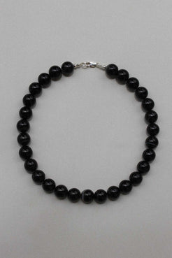 Black agate beaded necklace with sterling silver clasp, laid in a circle on a soft grey background.