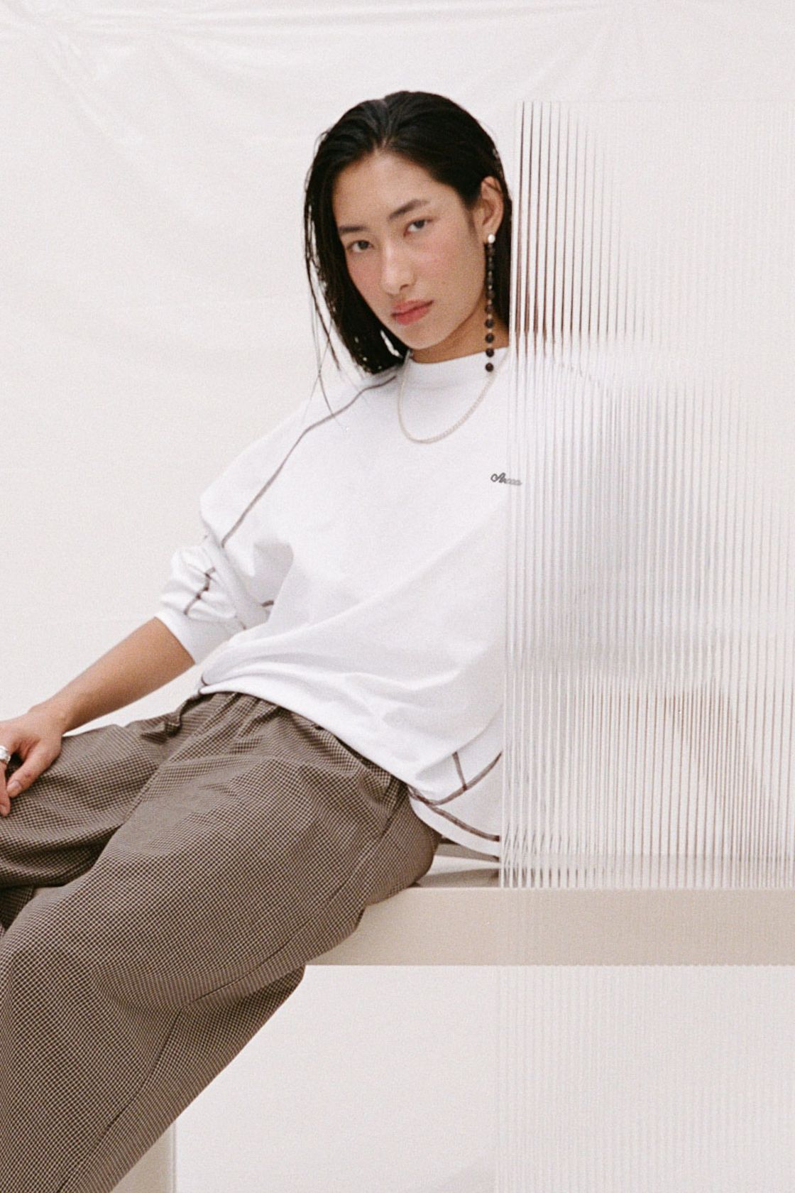 Model wearing the Kesh tee in cream behind a layer of plexiglass. 