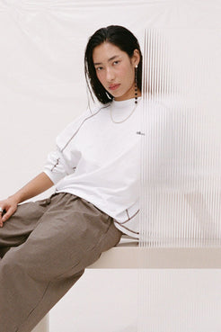 Model wearing the Kesh tee in cream behind a layer of plexiglass. 