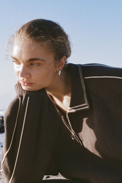 Lifestyle close-up of brown sweater worn outdoors showing collar and zip detail