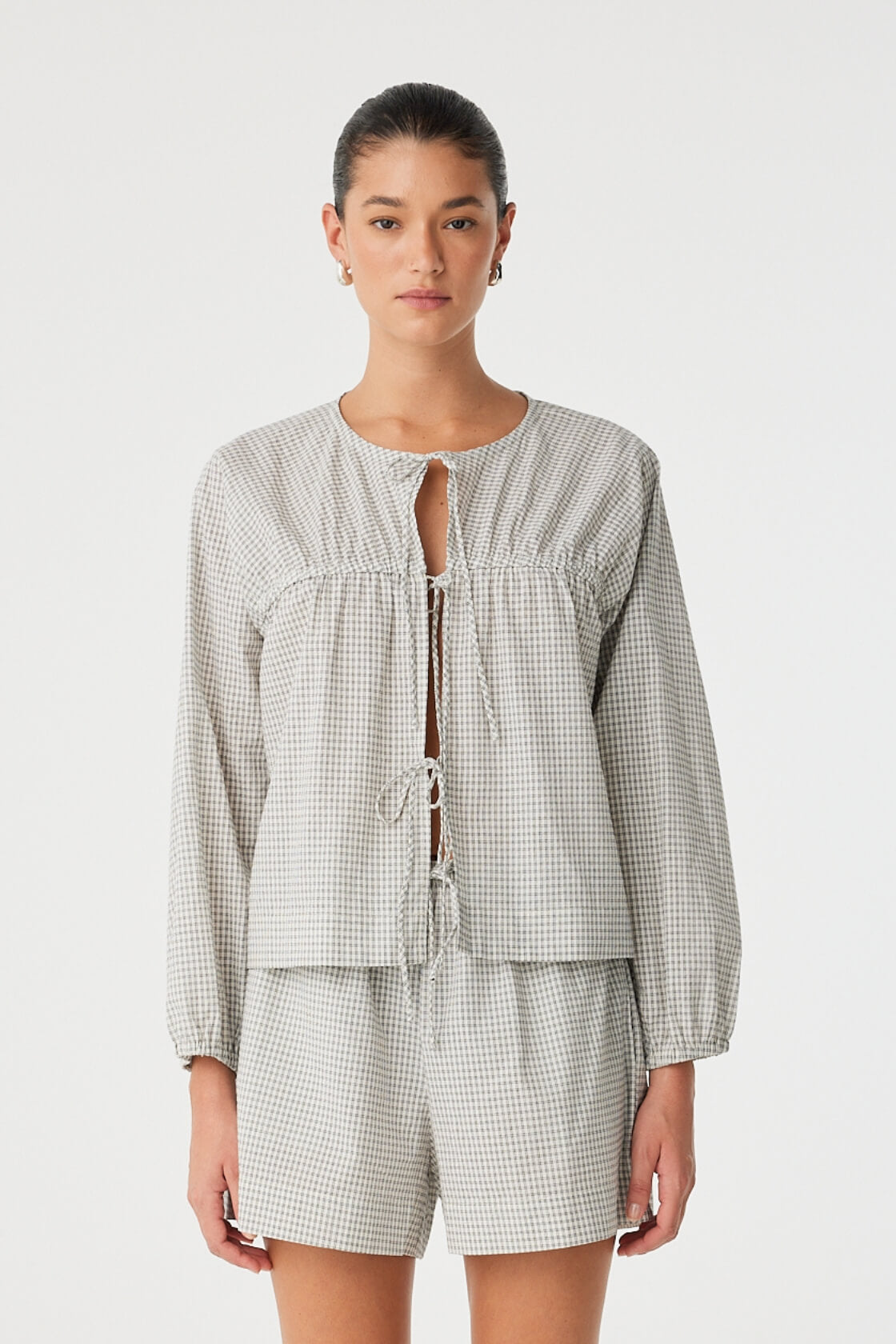 Model wears a relaxed-fit cotton blouse in black check with tie-front closure and soft gathers—styled with matching shorts for an effortless set.