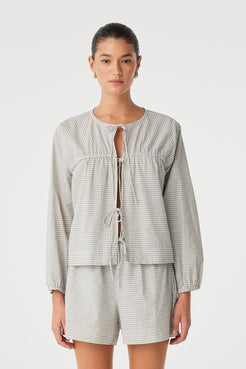 Model wears a relaxed-fit cotton blouse in black check with tie-front closure and soft gathers—styled with matching shorts for an effortless set.