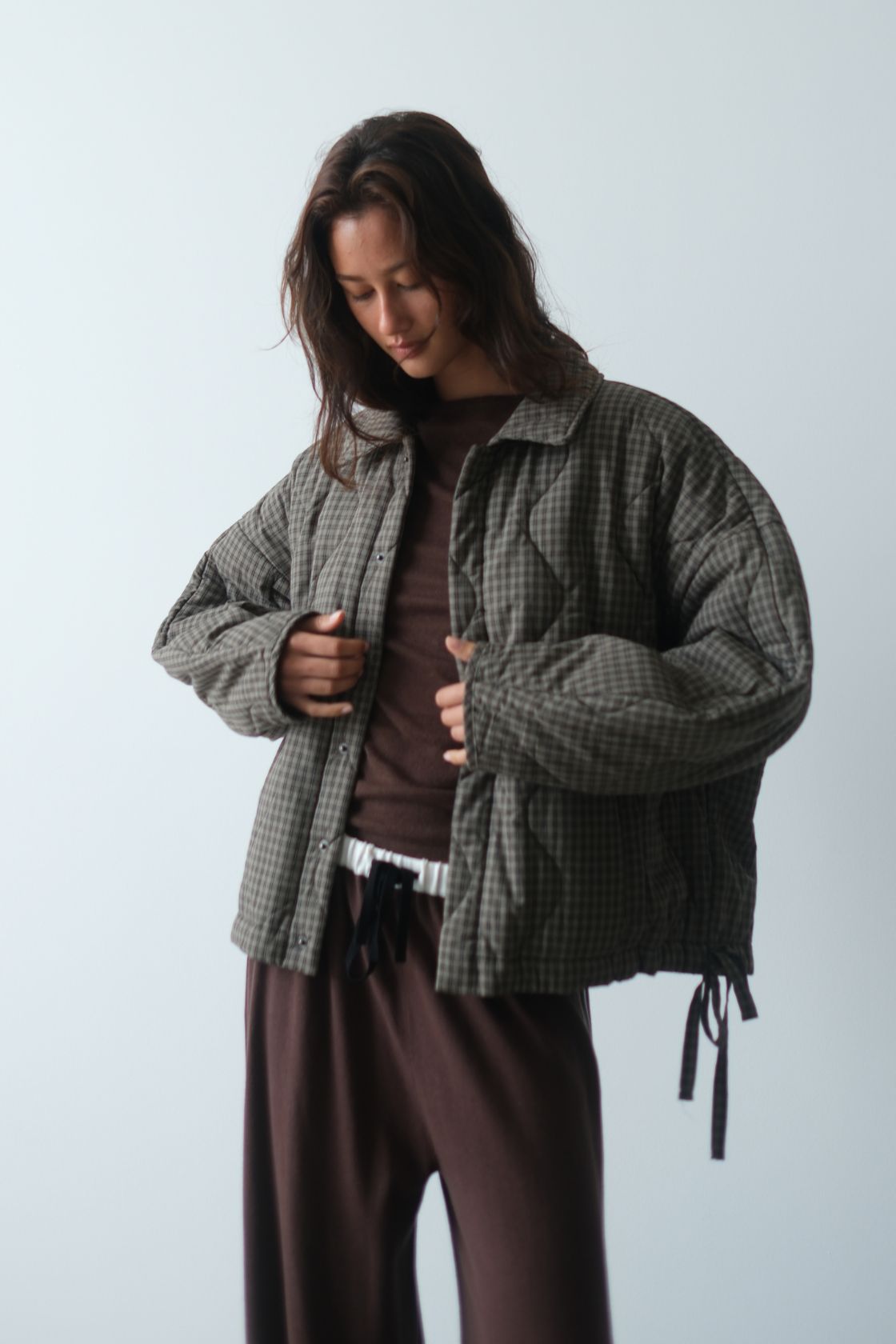 Studio image of the Matteo Jacket in Olive & Teal Check, styled open with a chocolate brown top and matching lounge pants, showing the slouchy fit, padded sleeves and adjustable hem ties.
