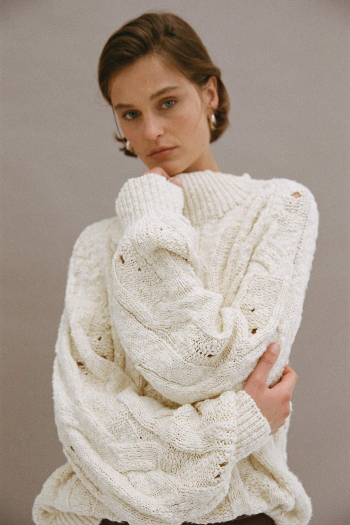 Close-up front view of cream chunky cable knit sweater with funnel neck