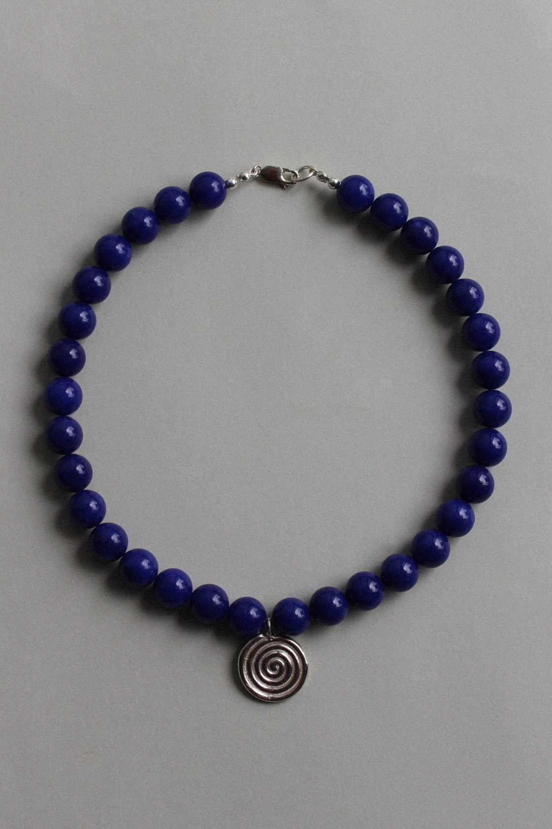 Blue chalcedony beaded necklace with recycled sterling silver Eddy Swirl pendant, laid in a circle on a soft grey background.