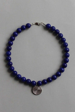 Blue chalcedony beaded necklace with recycled sterling silver Eddy Swirl pendant, laid in a circle on a soft grey background.