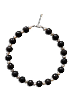 A beaded necklace featuring alternating large glossy black beads and smaller matte off-white beads, completed with a silver-tone lobster clasp, shown on a plain white background.