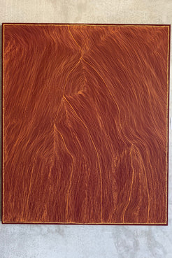 A square wooden board or panel with a rich reddish-brown wood grain pattern, photographed flat against a light gray textured background.