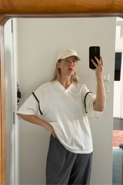 White knit top with contrast piping styled with grey pants in mirror