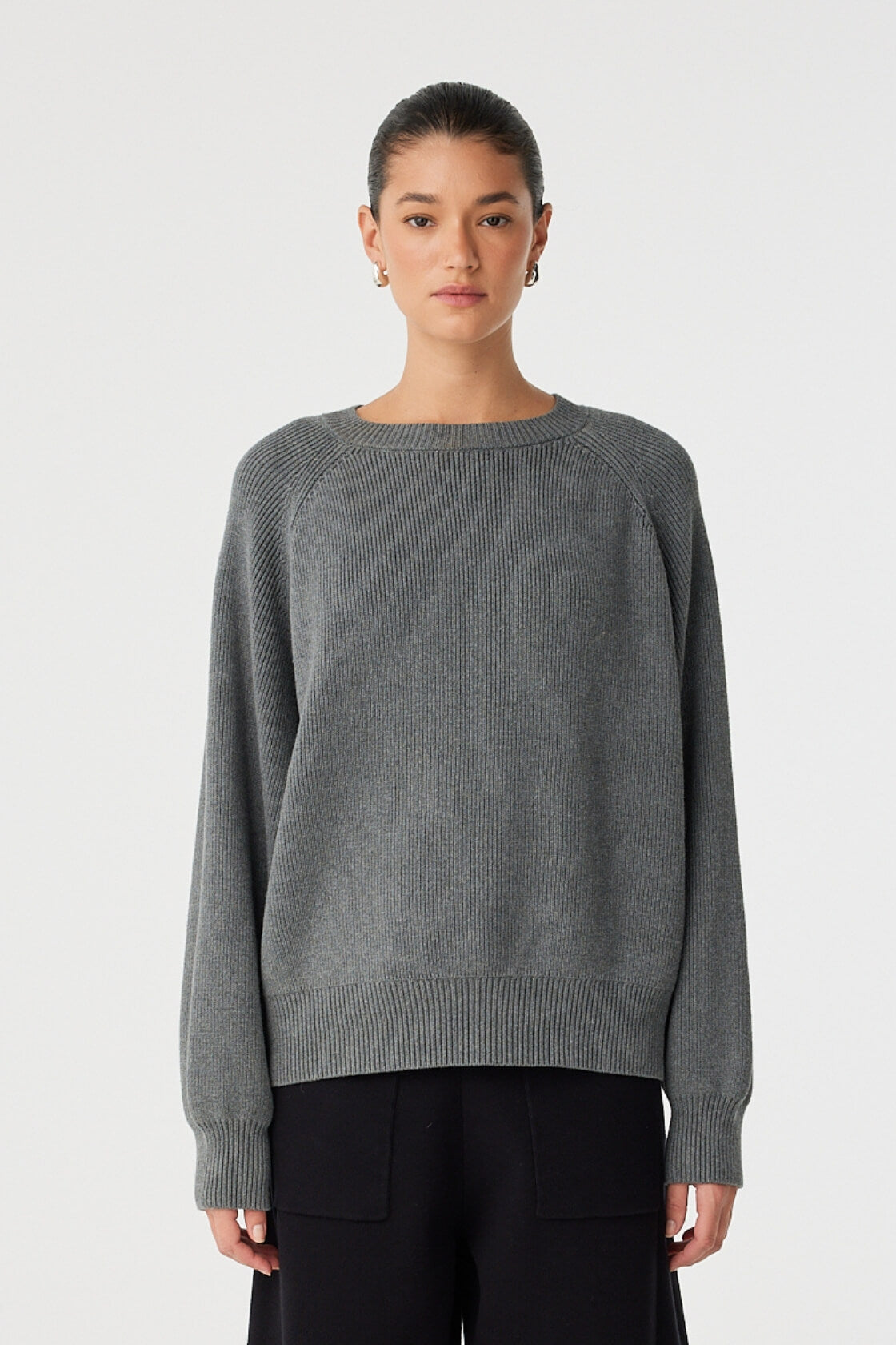 Model wears oversized raglan sweater in dark grey marle, with ribbed hem and cuffs.