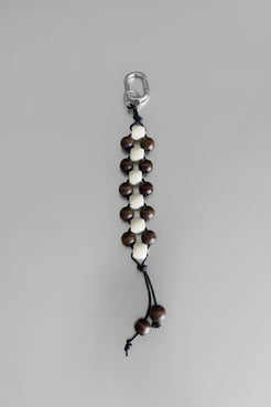 Close-up of neutral timber bead keychain in cream and chocolate tones with leather cord and silver hardware.