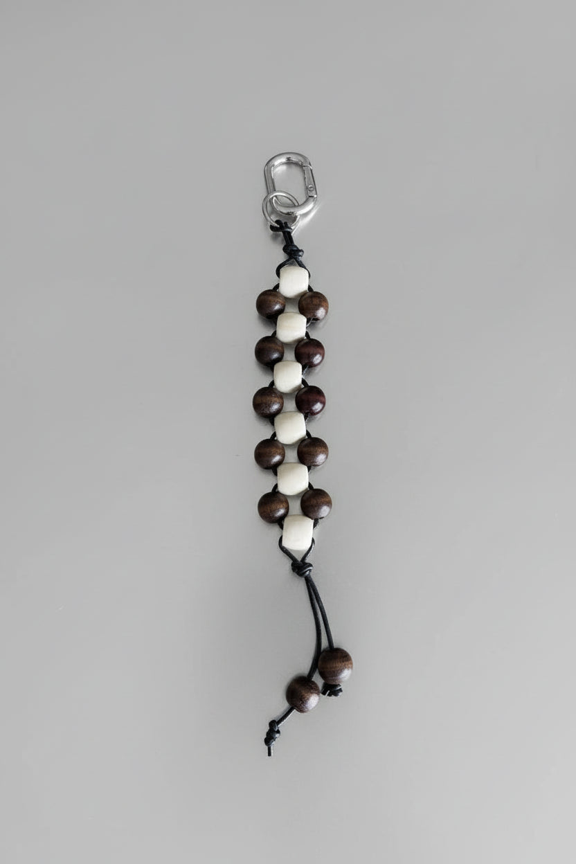 Close-up of neutral timber bead keychain in cream and chocolate tones with leather cord and silver hardware.