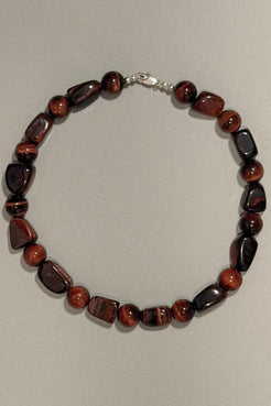 A beaded necklace made of polished reddish-brown and black gemstone beads with a silver clasp, displayed on a neutral light gray background.