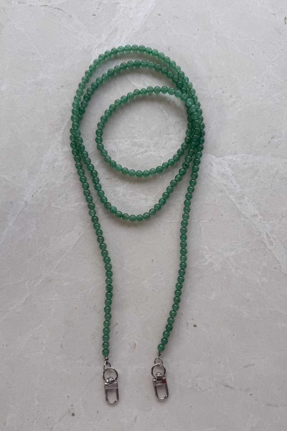 Hand-strung green aventurine crystal beaded phone carrier with clear loop attachment, coiled to show soft green tones and natural variations.