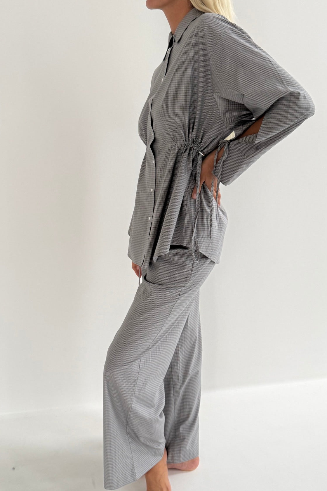 A woman modeling a matching blue and white striped two-piece loungewear set, featuring a long-sleeve button-front top with a tie waist and matching wide-leg pants, set against a plain white studio background.
