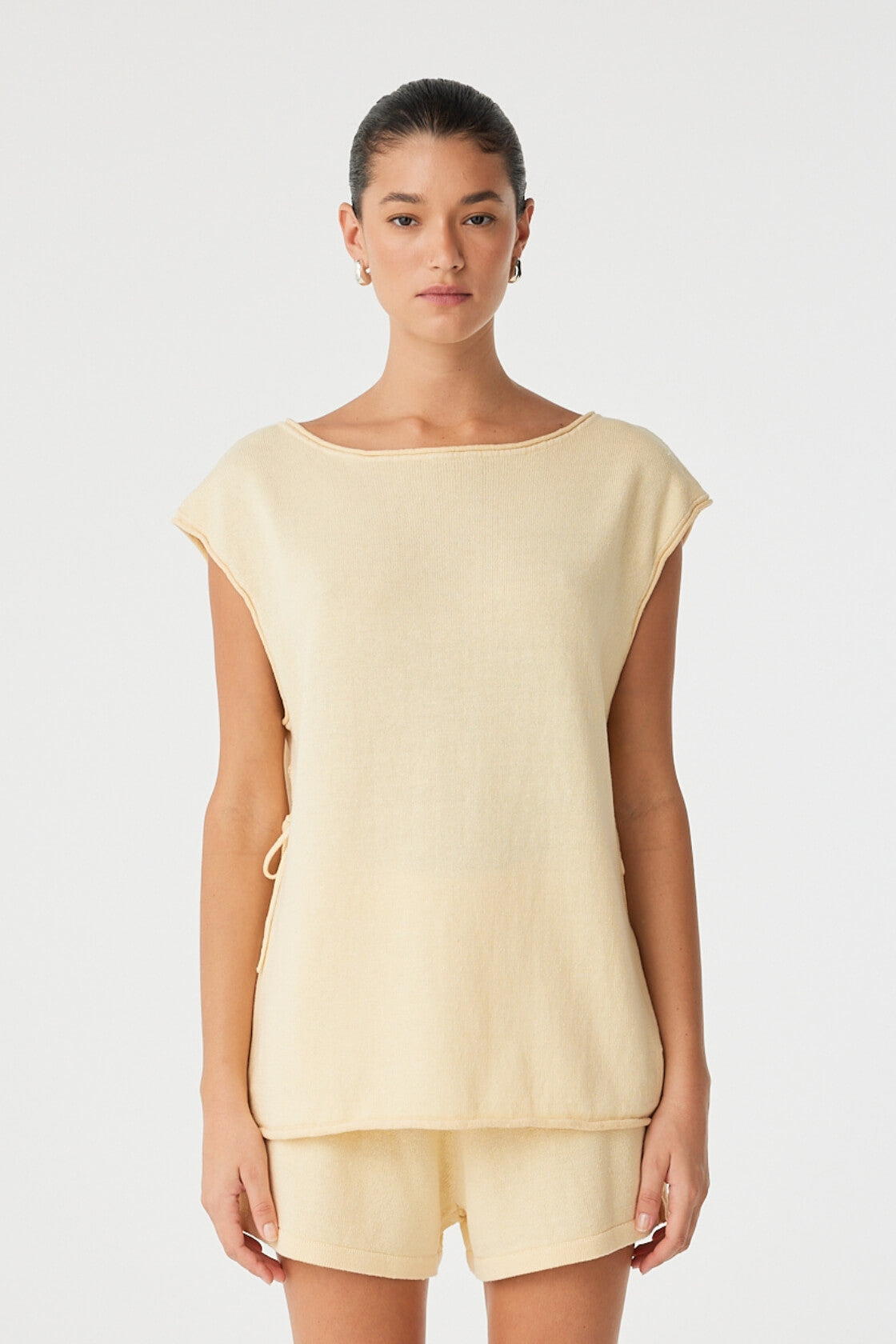 Model wears oversized sleeveless top in butter yellow linen–cotton with tie side detail.