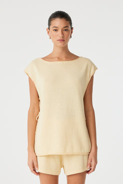 Model wears oversized sleeveless top in butter yellow linen–cotton with tie side detail.