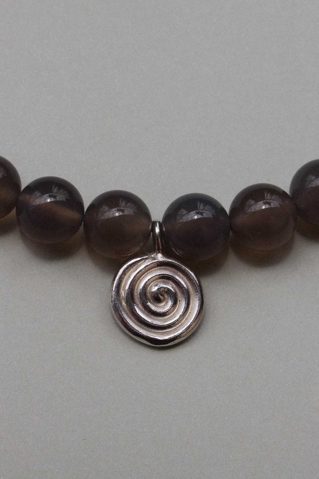 Close-up of taupe grey agate beads with a recycled sterling silver Eddy Swirl pendant on a minimal beaded necklace.