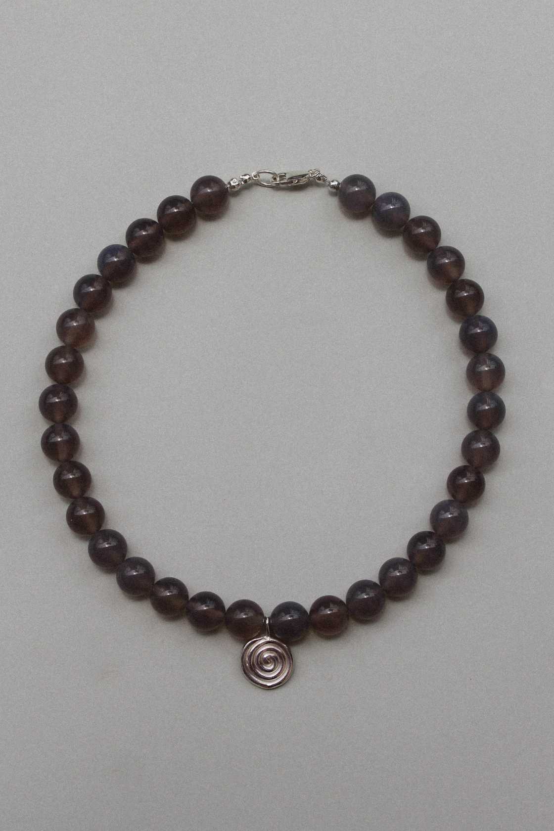 Taupe grey agate beaded necklace with recycled sterling silver Eddy Swirl pendant, laid in a circle on a soft grey background.