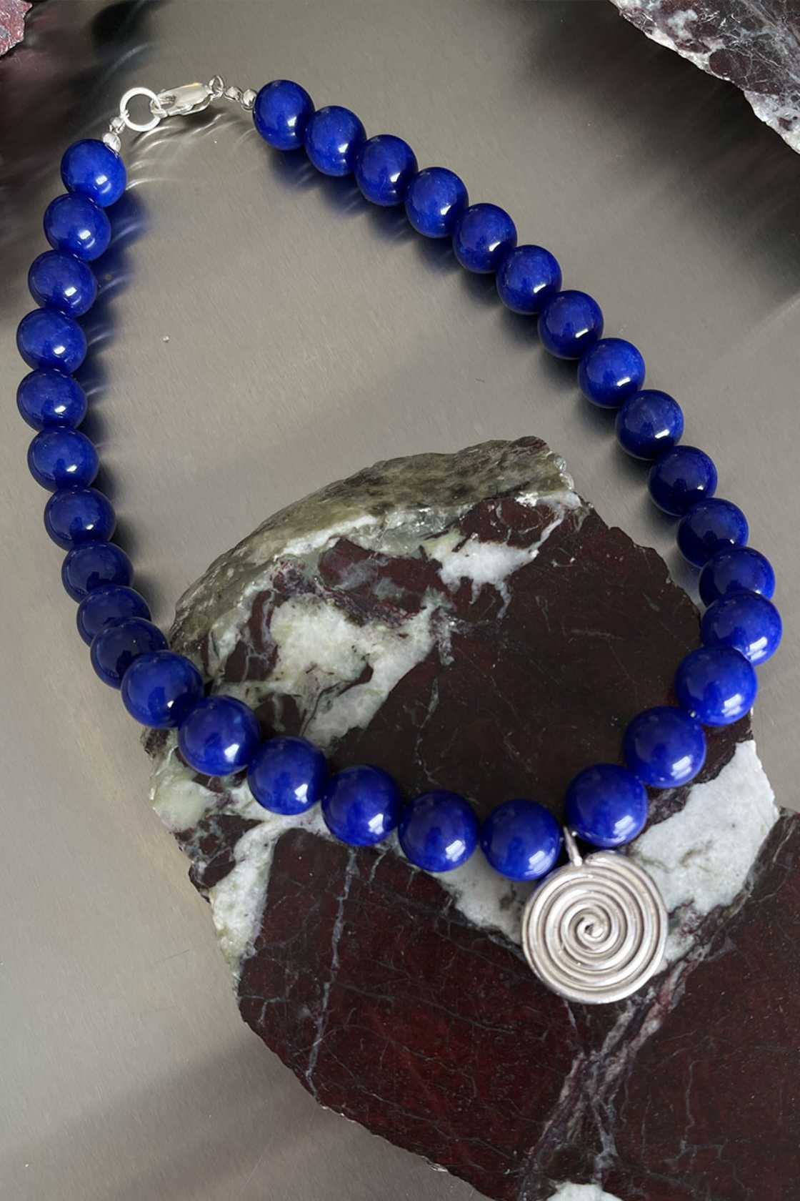 Blue chalcedony necklace with sterling silver Eddy Swirl pendant and clasp, draped over a textured stone surface for a minimal styled shot.