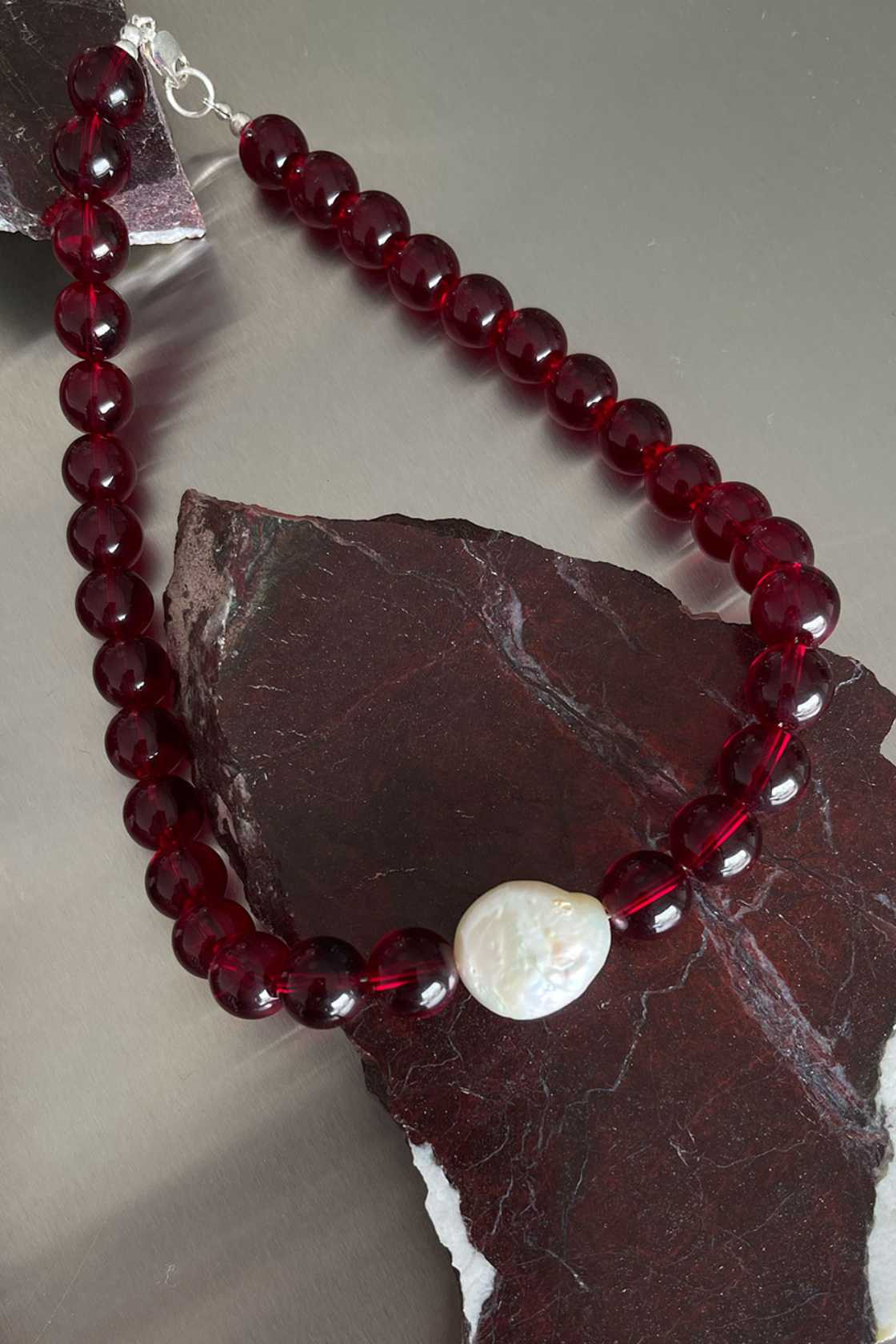 Red garnet necklace with freshwater pearl detail and sterling silver clasp, styled draped over a dark stone surface.
