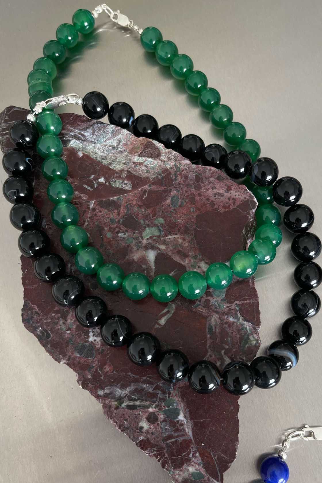 Black agate beaded necklace layered with a green chalcedony strand, draped over a textured stone for a minimal styled composition.