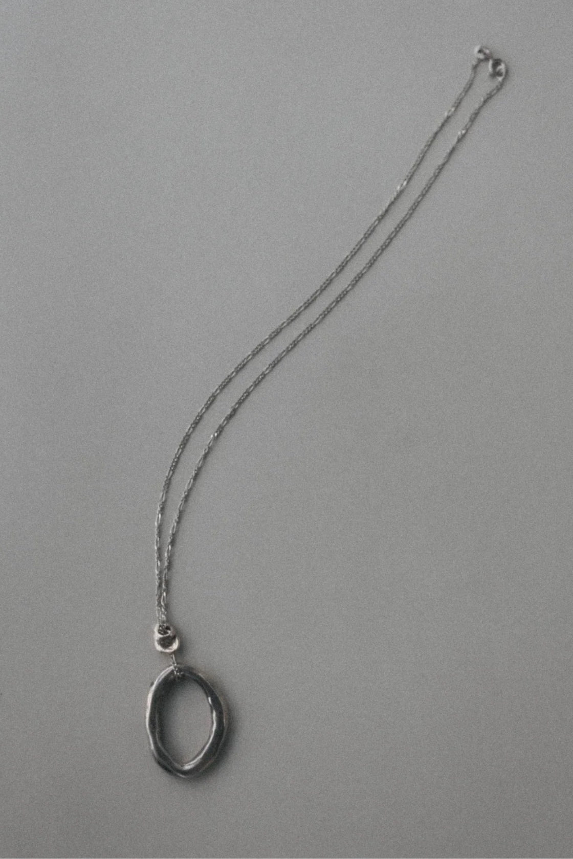 A silver-toned necklace featuring a textured, open oval pendant, displayed on a plain gray background.