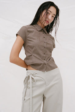 Model wearing the Freya button-up shirt in chocolate check tucked into light sage drawstring trousers, photographed against a white studio backdrop.