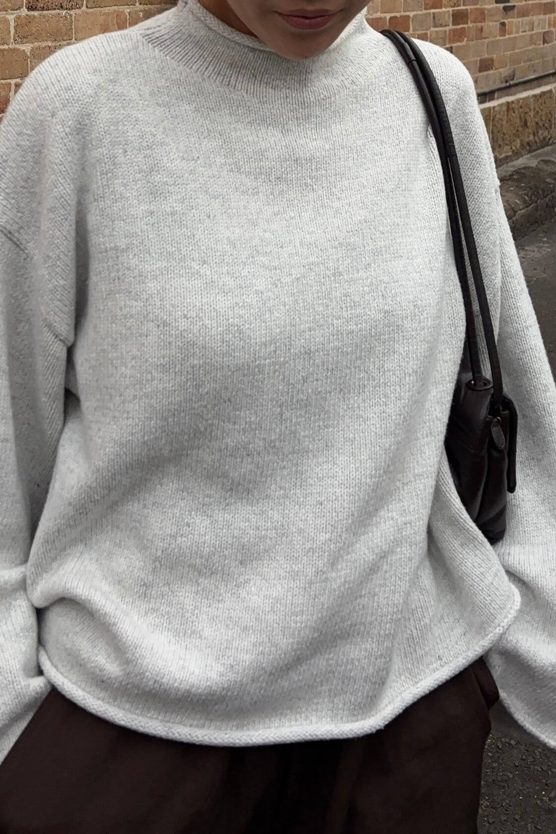 Close-up detail view of the Maeve Sweater in snow marle highlighting the soft marled knit texture, relaxed drape through the body and rolled hem and neckline finish styled with espresso pants