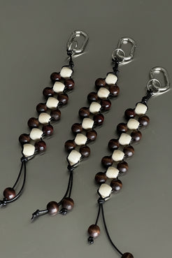 cream and chocolate timber beaded keychain with leather cord tassel and silver clasp, styled on a dark surface.