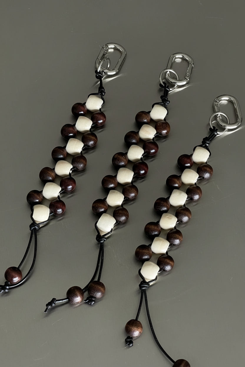 cream and chocolate timber beaded keychain with leather cord tassel and silver clasp, styled on a dark surface.