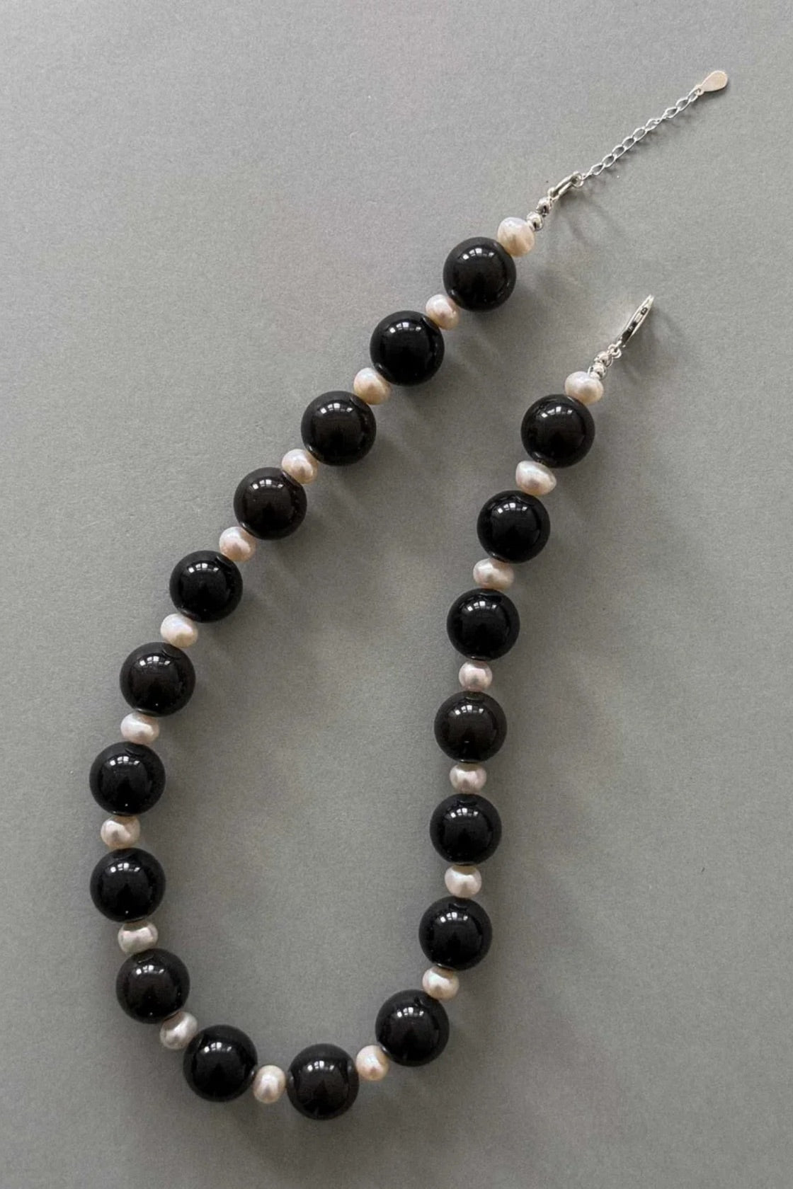 A beaded necklace featuring glossy black round beads alternating with small white pearl-like beads, displayed on a neutral gray background.
