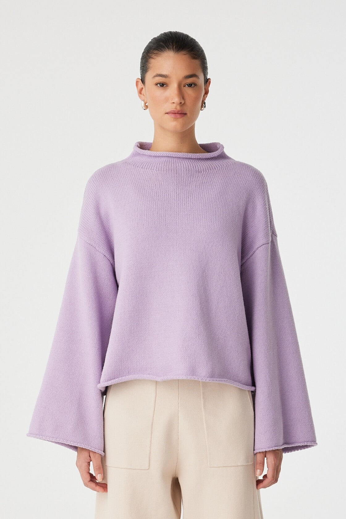 Model wears cropped lilac funnel-neck sweater with wide sleeves and soft relaxed shape.