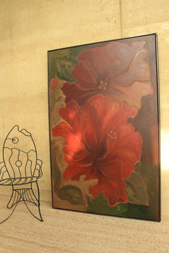 A framed painting of two large red and burgundy flowers with green leaves, leaning against a beige wall next to a black wire fish-shaped chair.