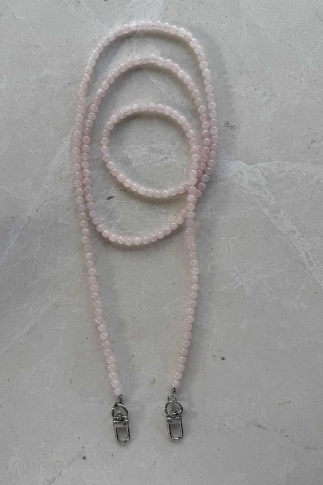 Hand-strung rose quartz crystal beaded phone carrier with clear loop attachment, coiled to show soft blush tones and natural variations.